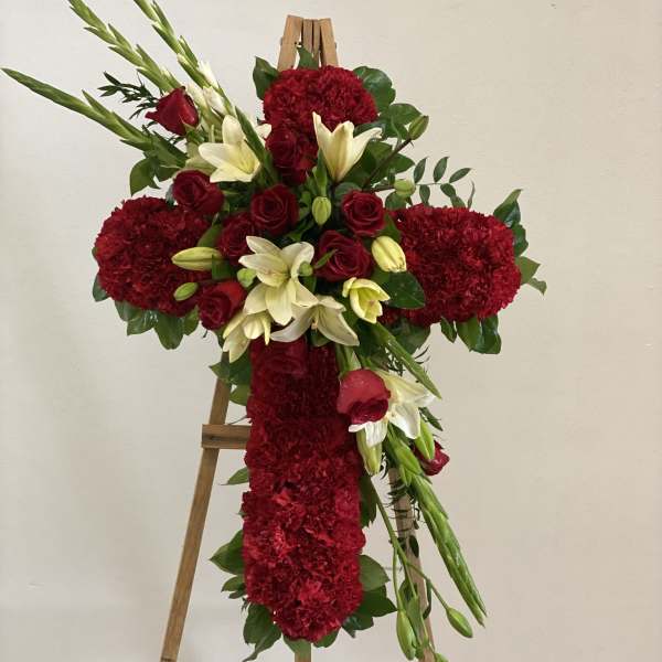 Red floral cross arrangement on a wooden easel with white lilies and roses