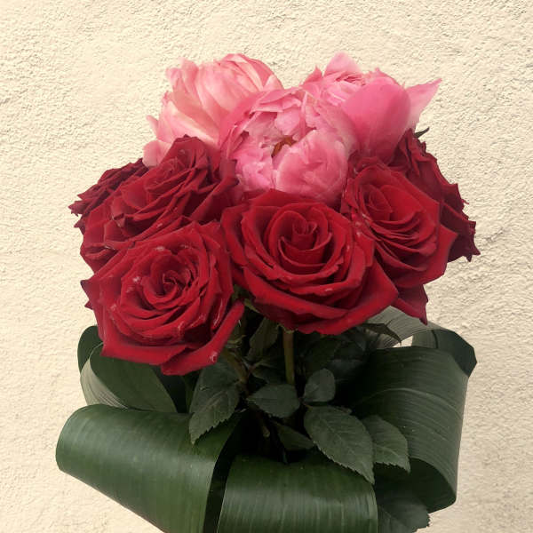 Red and pink roses arranged in a clear glass vase with a red ribbon
