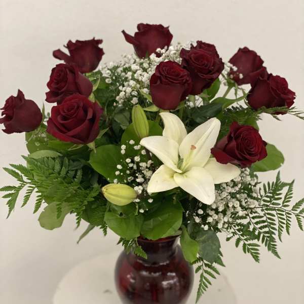 Red roses and a white lily arranged in a burgundy vase