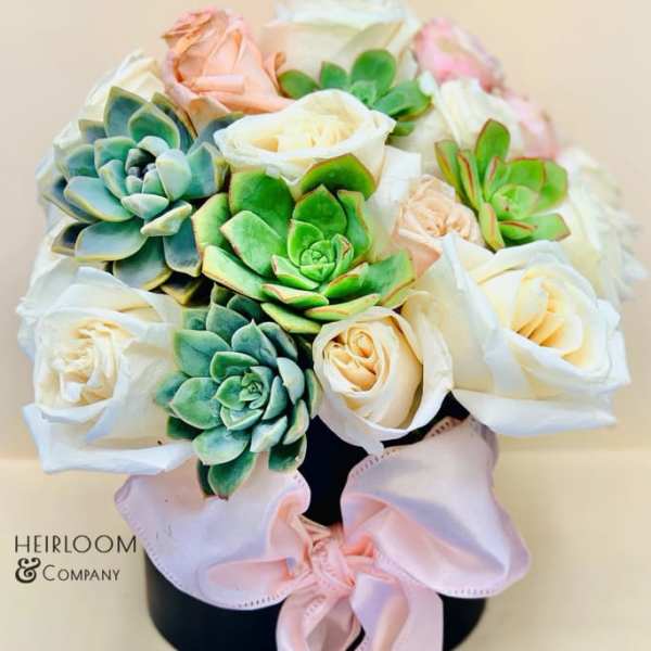 Bouquet of white roses and succulents in a black hat box with a pink ribbon