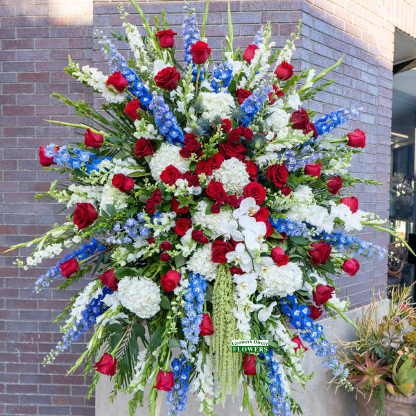 Tall standing spray with red roses, white hydrangeas and orchids, and blue delphinium on an easel