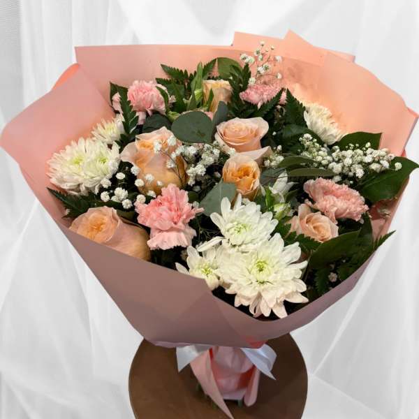 Bouquet of peach roses, pink carnations, and white chrysanthemums wrapped in pink paper