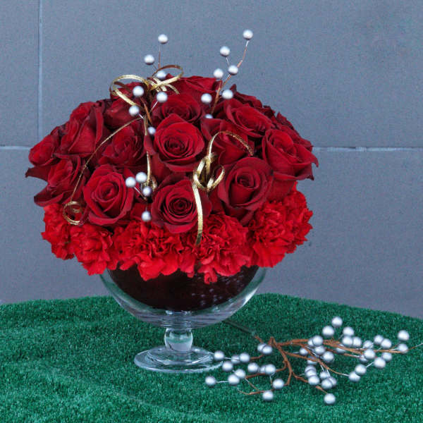 Red roses and carnations in a glass compote with gold ribbon and white berry picks