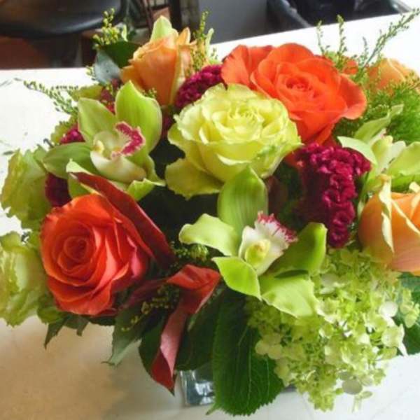 Mixed bouquet of orange and green roses with orchids in a glass vase