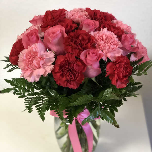 Arrangement of pink roses and red and pink carnations in a clear vase with a pink ribbon