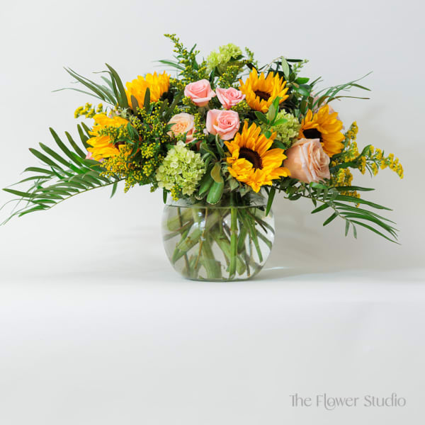 Low round arrangement of yellow sunflowers and pink roses in a clear glass bowl vase