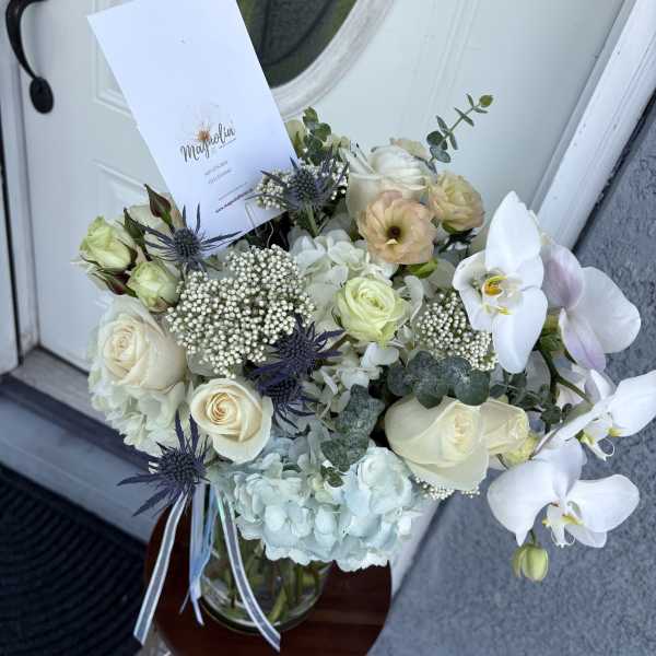 Bouquet of white roses, orchids, and pale hydrangeas in a glass vase