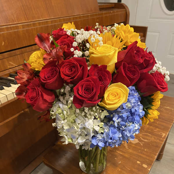 Bouquet of red and yellow roses with blue and white hydrangeas in a glass vase