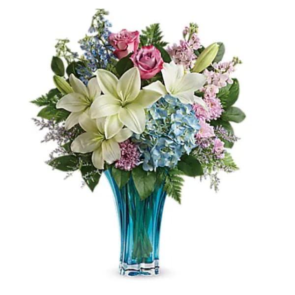 Bouquet of lilies, roses, hydrangeas, and mixed blooms in a blue glass vase