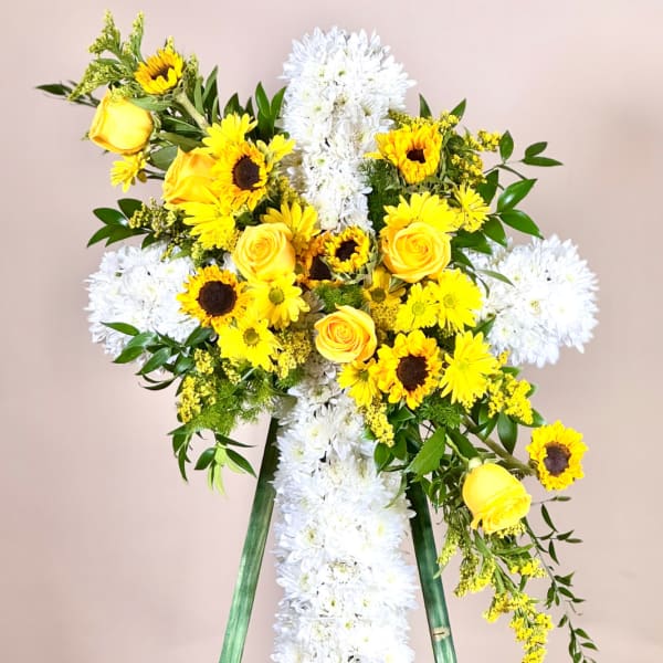 Yellow roses and sunflowers arranged on a white floral cross easel.