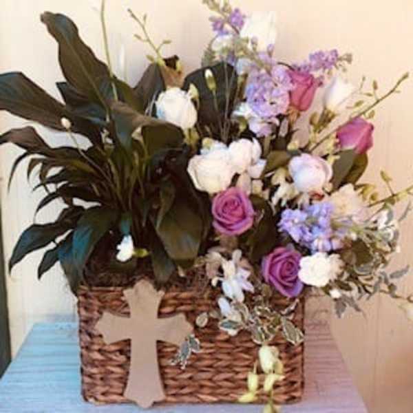 Basket arrangement of purple and white flowers with a cross decoration