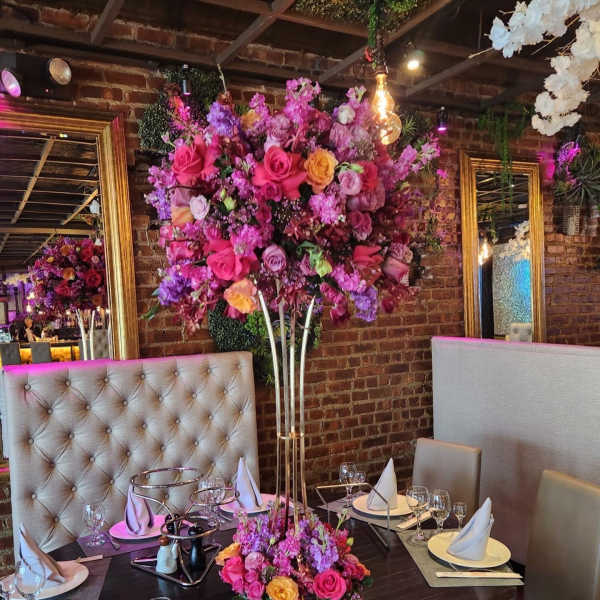 Tall floral centerpiece with pink, purple, and yellow flowers on a dining table