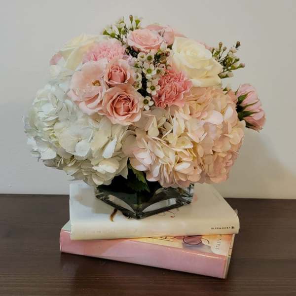 Pink and white floral arrangement in a glass vase on stacked books