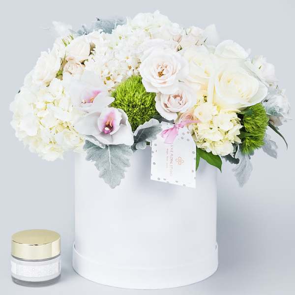 White floral arrangement in a round hat box with a small candle beside it.