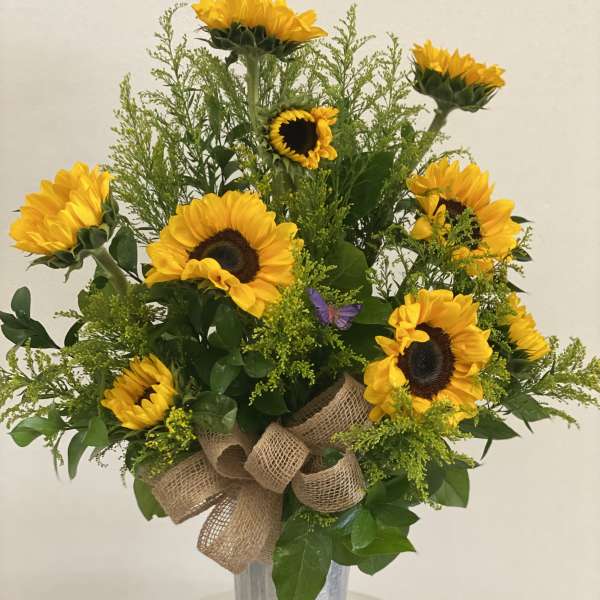 Sunflower arrangement in a tall silver vase with a burlap bow