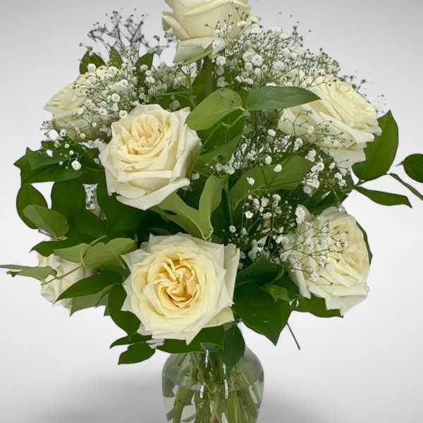 Cream roses arranged in a clear glass vase with baby's breath