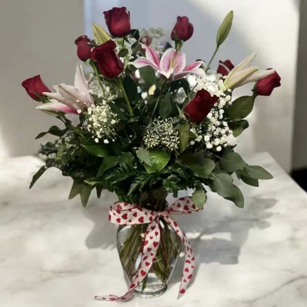 Bouquet of red roses and pink lilies in a glass vase with a heart ribbon
