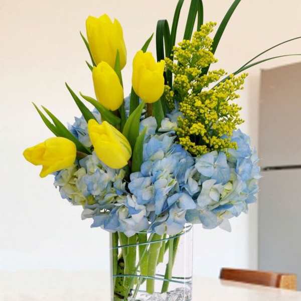 Yellow tulips and blue hydrangeas in a clear glass vase