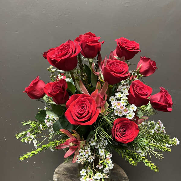 Red roses arranged in a clear glass vase with small white filler flowers