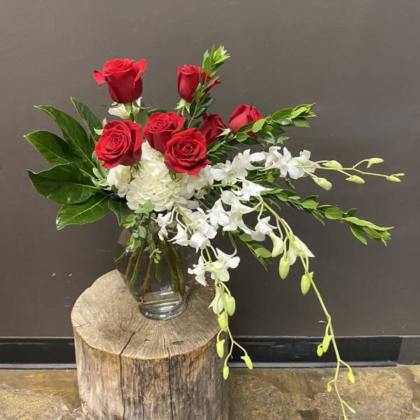 Red roses and white orchids in a glass vase on a wood stump