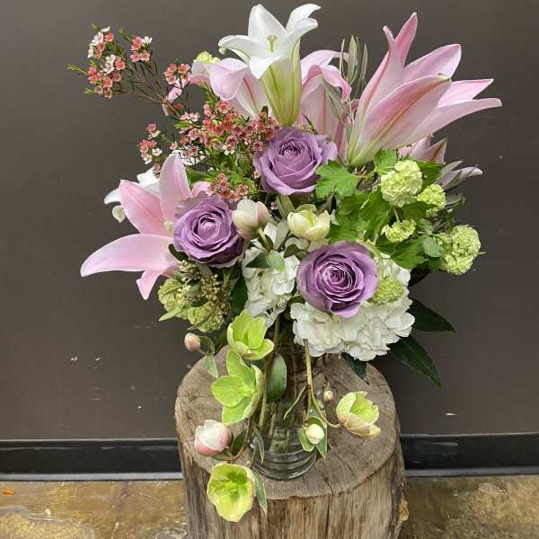 Bouquet of pink lilies, lavender roses, and white hydrangea in a glass vase