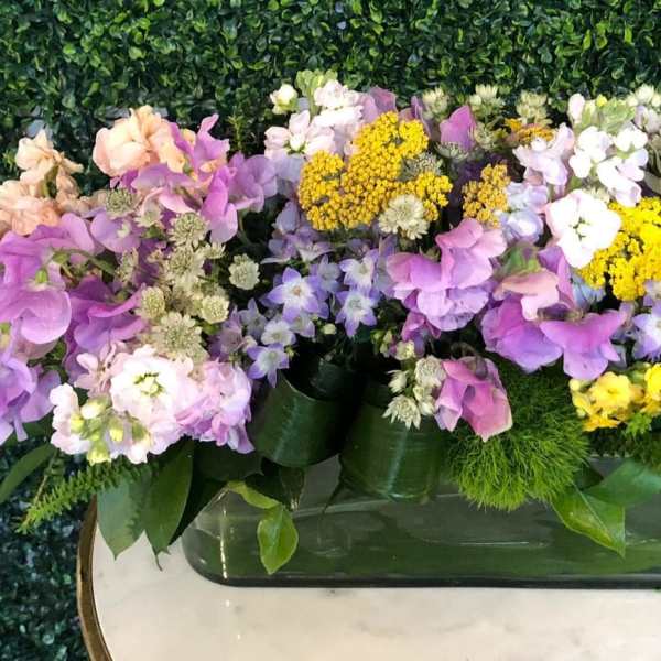 Mixed bouquet of purple, pink, white, and yellow flowers in a low rectangular vase