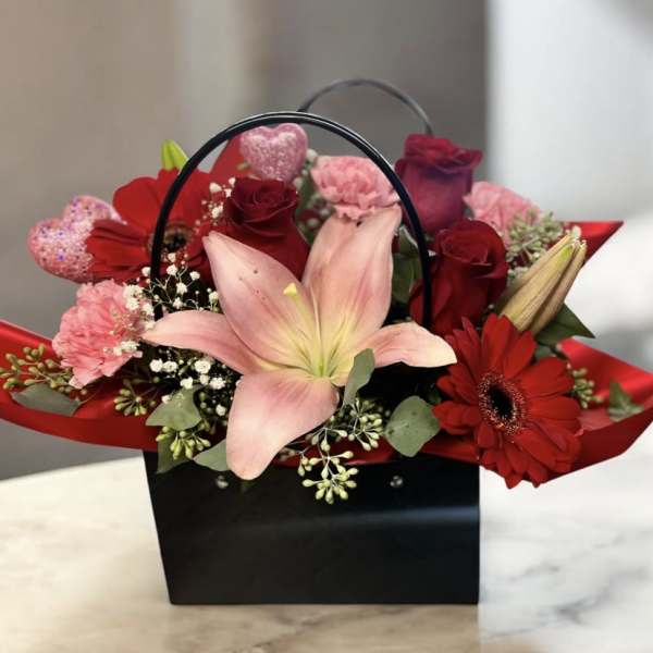 Red and pink flower arrangement in a black handled gift box