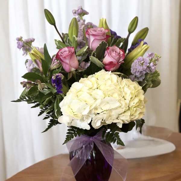 Pink roses and white hydrangeas in a purple vase with a ribbon