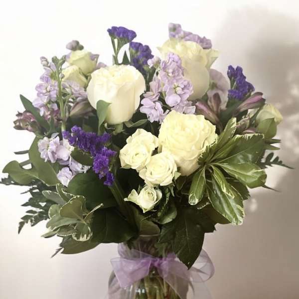 Bouquet of white roses and purple flowers in a glass vase