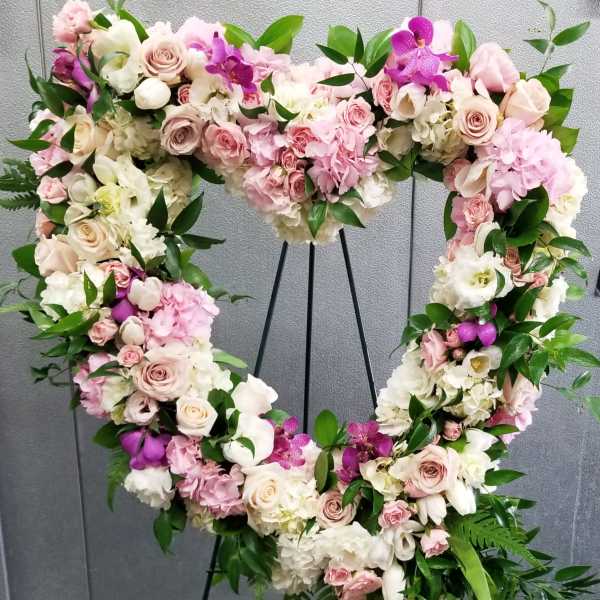 Heart-shaped floral wreath with pink and white roses on a stand