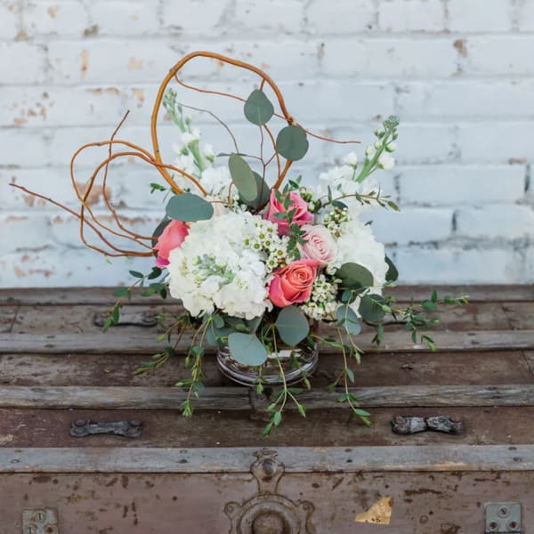 Pink and white floral arrangement in a glass vase with curly branches