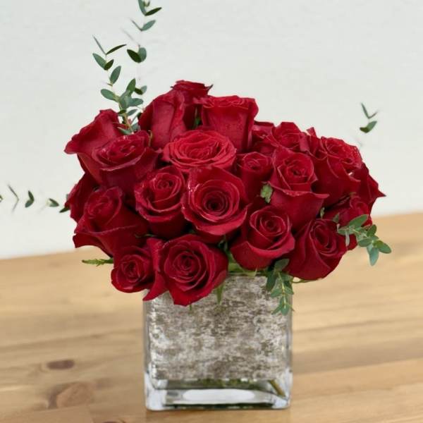 Red roses arranged in a square glass vase with a few eucalyptus stems