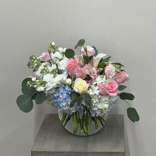 Pink and white roses with blue hydrangeas in a clear round vase