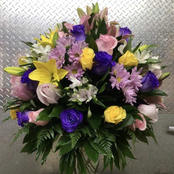 Mixed bouquet of lilies, roses, and daisies in a clear glass vase