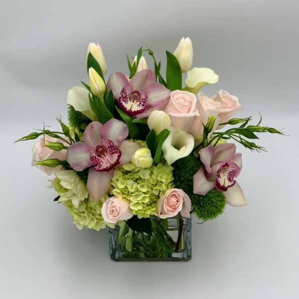 Pink orchids, roses, calla lilies, and tulips in a glass vase
