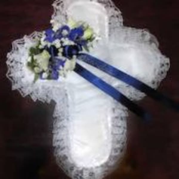 White cross-shaped cushion with blue and white flowers and long dark blue ribbons.