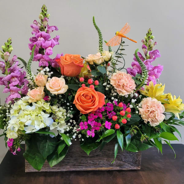 Rectangular wooden box filled with orange roses, pink carnations, purple snapdragons, and yellow blooms