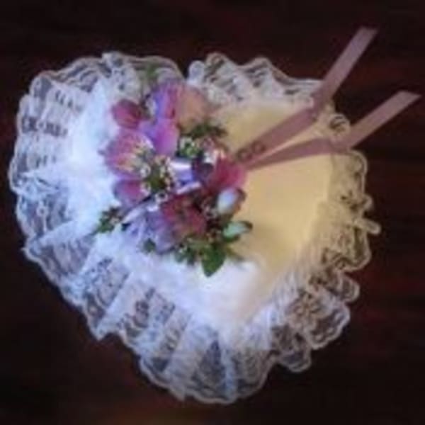 Heart-shaped white lace pillow with small purple floral spray and ribbons
