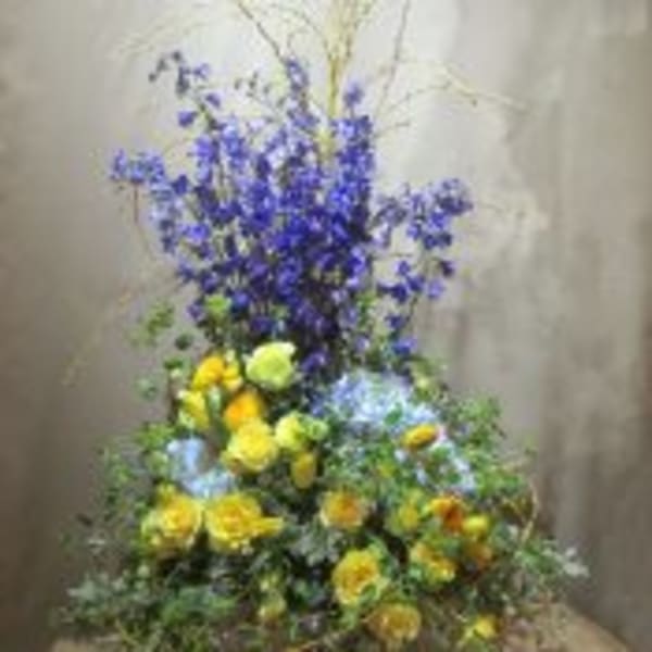 Tall arrangement with yellow roses and blue delphinium in a low basket container