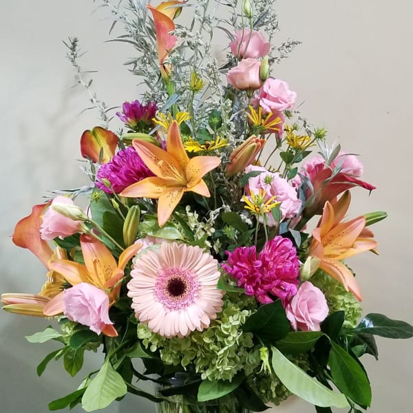 Tall mixed bouquet of lilies, gerbera, hydrangea, and calla lilies in a clear glass vase