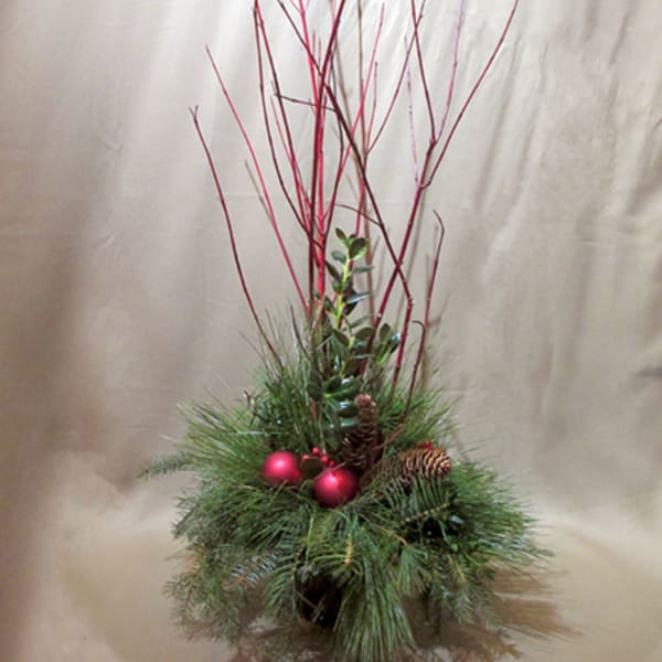 Tall winter arrangement with red branches, evergreen foliage, pinecones, and red ornaments.