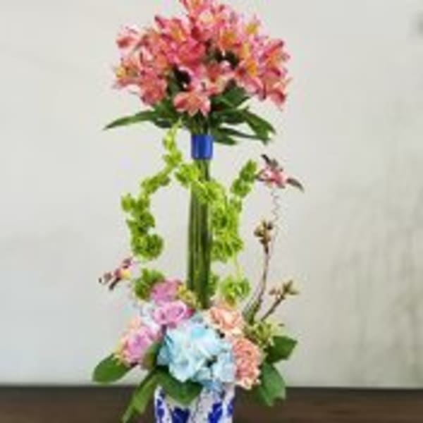 Tall arrangement with pink alstroemeria, Bells of Ireland, and pastel roses in a blue and white vase