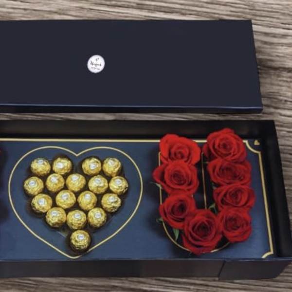 Black gift box with red roses and gold chocolates arranged in a heart