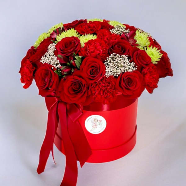 Red roses and carnations arranged in a red hat box with a ribbon