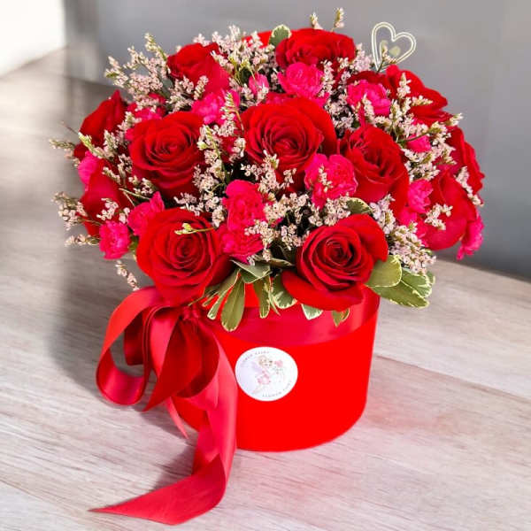Red roses and pink carnations in a red hatbox with ribbon
