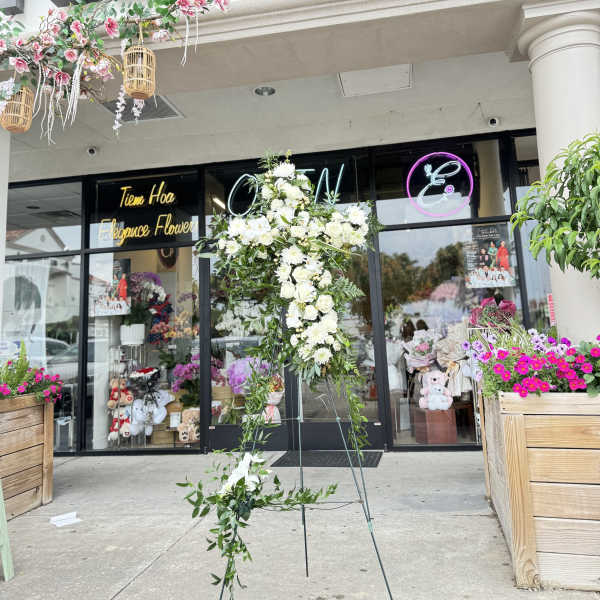 Tall white floral standing spray on an easel outside a flower shop