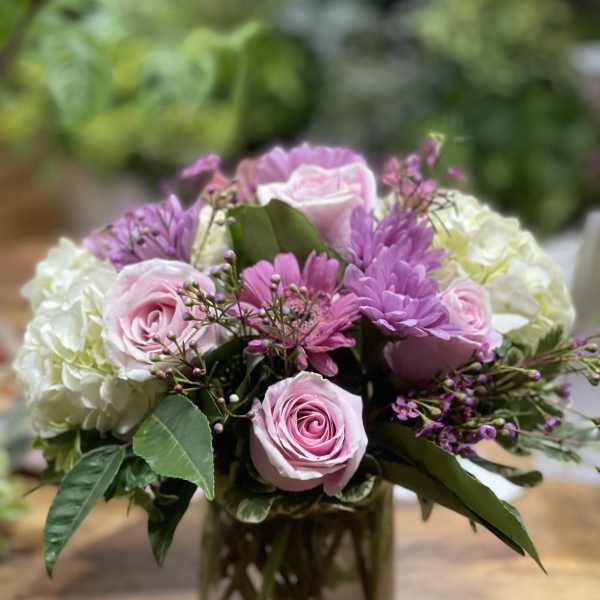 Pink roses and purple flowers arranged in a glass vase