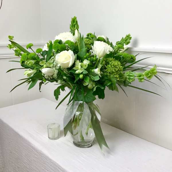 White and green floral arrangement in a glass vase with a ribbon