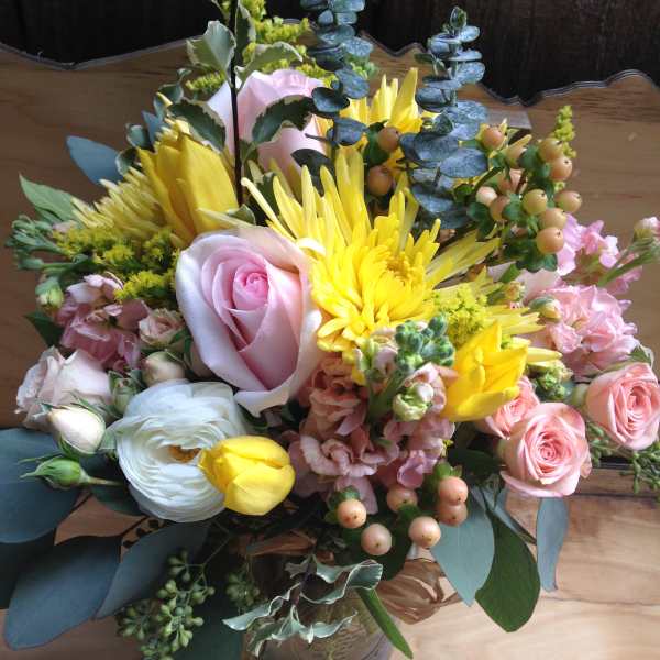 Mixed bouquet of pink roses, yellow blooms, and white flowers in a glass vase