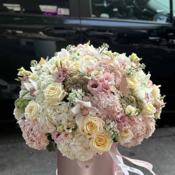 Large pastel bouquet of roses, hydrangeas, and orchids in a pink hat box